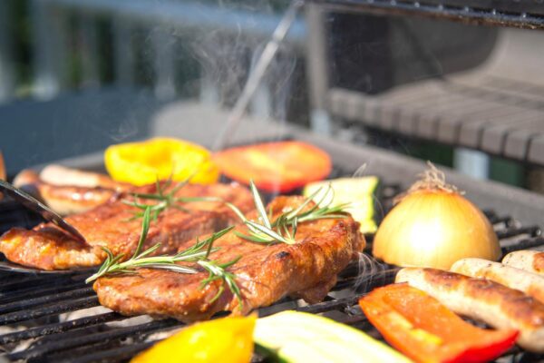 Closeup of someone grilling meat and vegetables. Outdoor grills are available at The Arno.